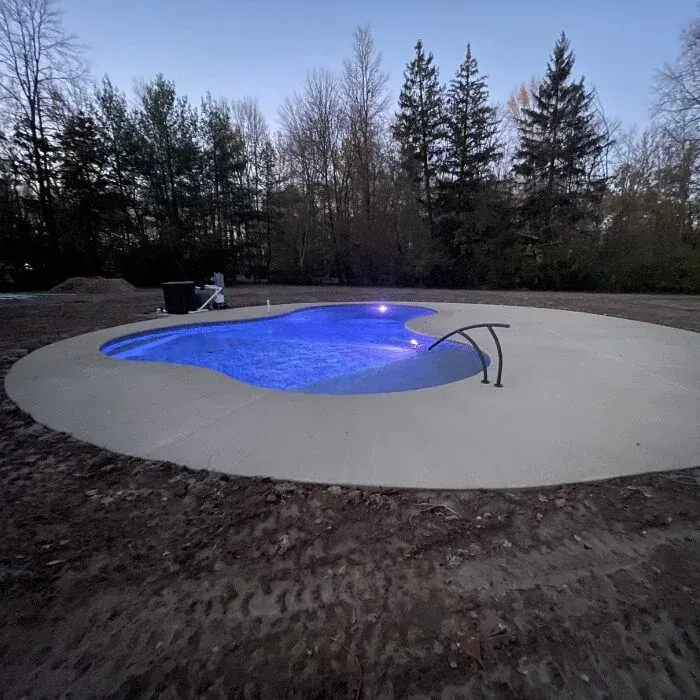 Concrete pool deck around a kidney-shaped pool lit blue at dusk