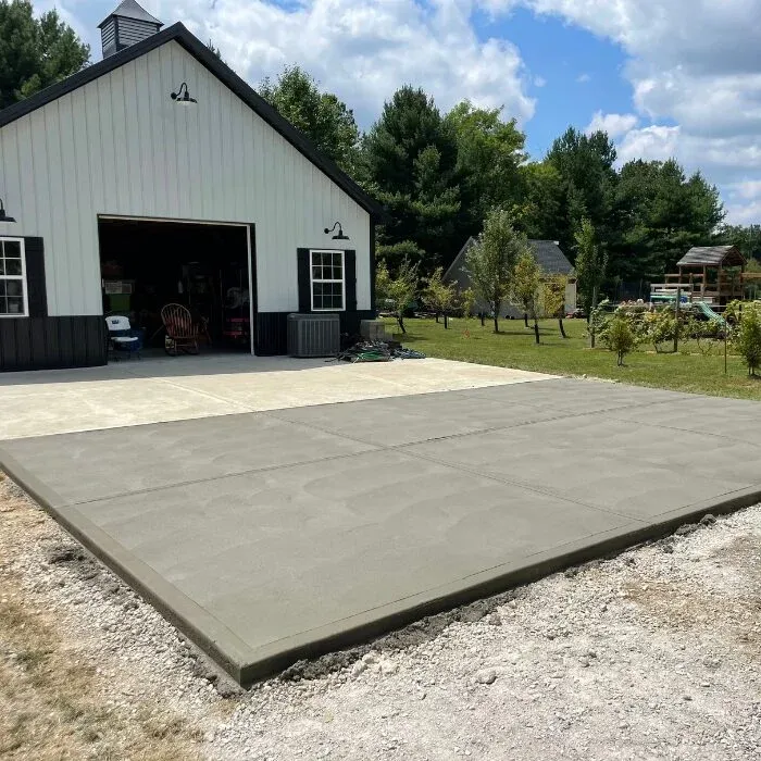Wide concrete driveway apron in front of a white pole barn garage