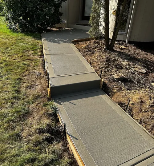 Freshly poured broom-finished concrete walkway with a step leading to a home entrance